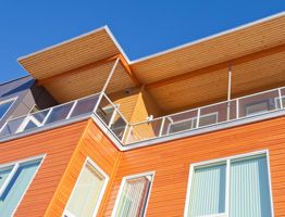 Exterior shot of a modern house with orange siding, white windows, and drawn shades.