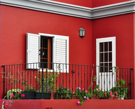 Exterior shot of a balcony with red walls, white window and door, and potted plants.